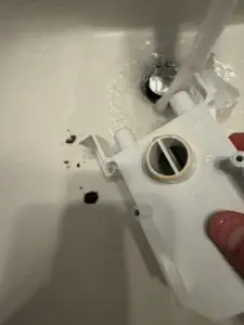 Furnace condensate trap being rinsed in a sink, with clumps of sludge that clogged it