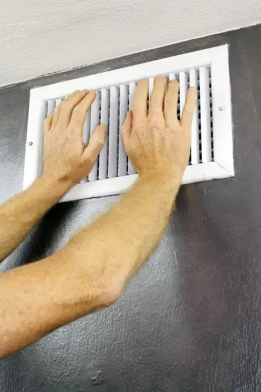 Hands in front of a air vent feeling to see if air is coming through